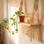 A finished macramé floating shelf with a pine board, knotted cotton cord hangers, and a trailing pothos plant mounted on a white wall.