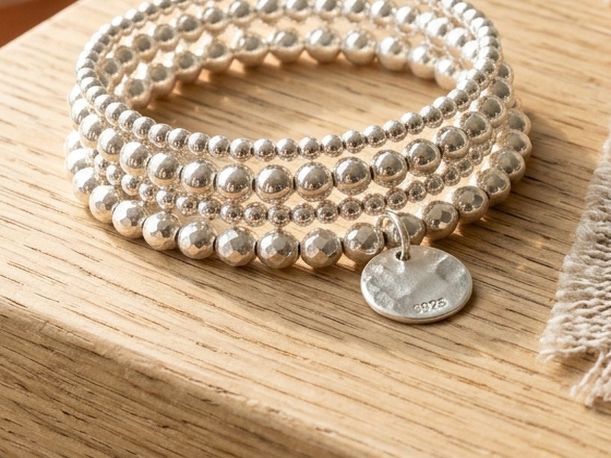 Macro detail of layered sterling silver beaded stretch bracelets featuring a delicate hammered disc charm with 925 stamp