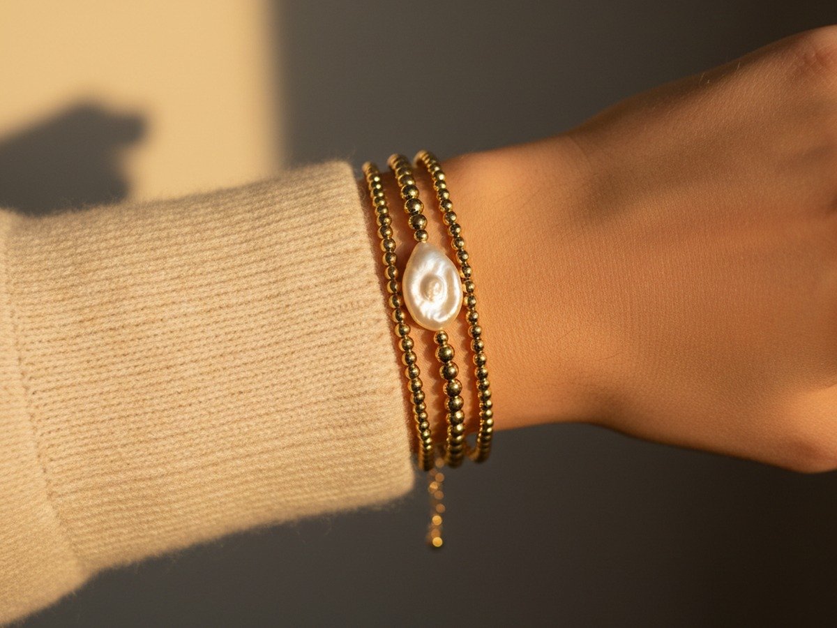 Aesthetic wrist stack of three 14k gold-filled beaded bracelets with pearl accent and knit sweater