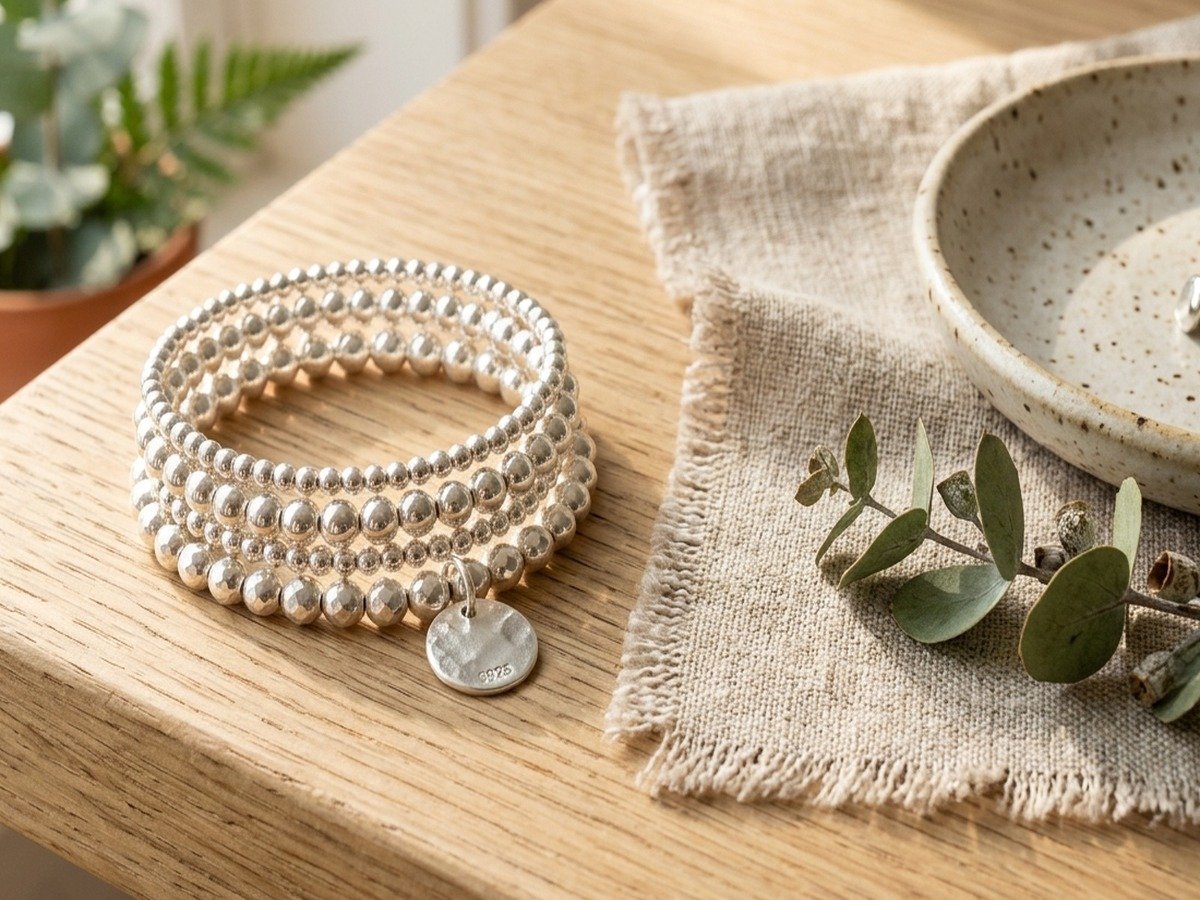 Boho jewelry display of handcrafted silver beaded bracelets styled alongside raw linen fabric, eucalyptus, and ceramic dish