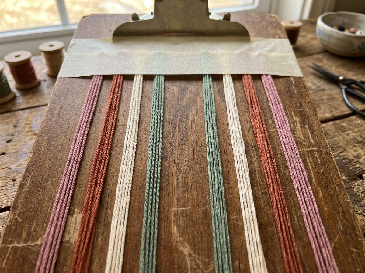 Organizing eight embroidery floss strands on a clipboard in mirrored order for the heart friendship bracelet pattern